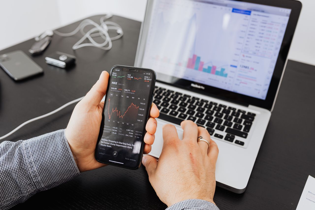 hero-img Person analyzes stock data with a smartphone and laptop, indoors.